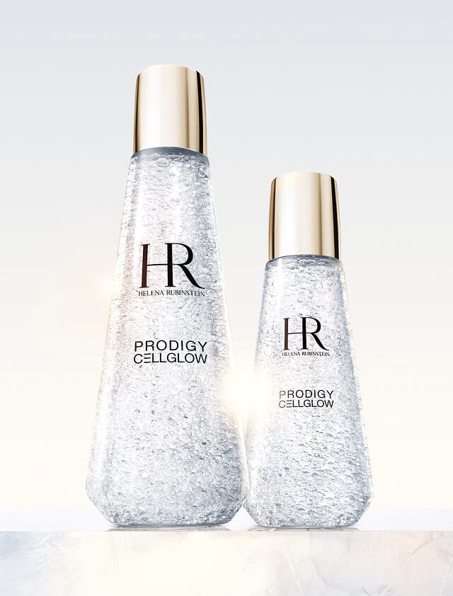 Dos frascos de suero transparentes Helena Rubinstein Prodigy Cellglow, uno grande y otro pequeno, llenos de burbujas hidratantes y con tapones dorados, sobre un fondo claro.