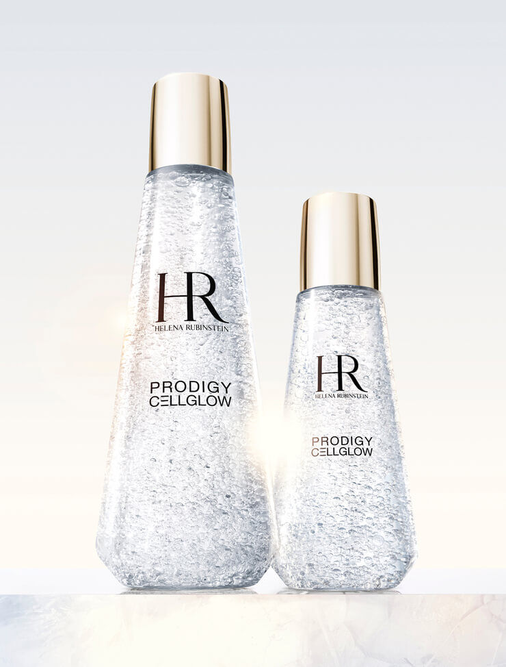 Dos frascos de suero transparentes Helena Rubinstein Prodigy Cellglow, uno grande y otro pequeno, llenos de burbujas hidratantes y con tapones dorados, sobre un fondo claro.