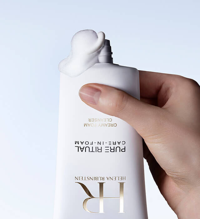 Una mano aprieta un bote de Pure Ritual Care-in-foam de Helena Rubinstein, del que sale una cantidad de producto.
