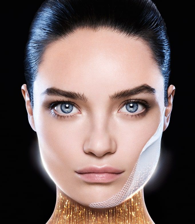 Rostro de mujer de ojos azules, con un parche fino en la mejilla. Bajo su barbilla, un resplandor dorado simboliza un efecto tensor o revitalizante. Fondo negro.