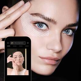 Modelo con piel radiante y mirada intensa, utilizando una aplicacion de maquillaje en su telefono movil.